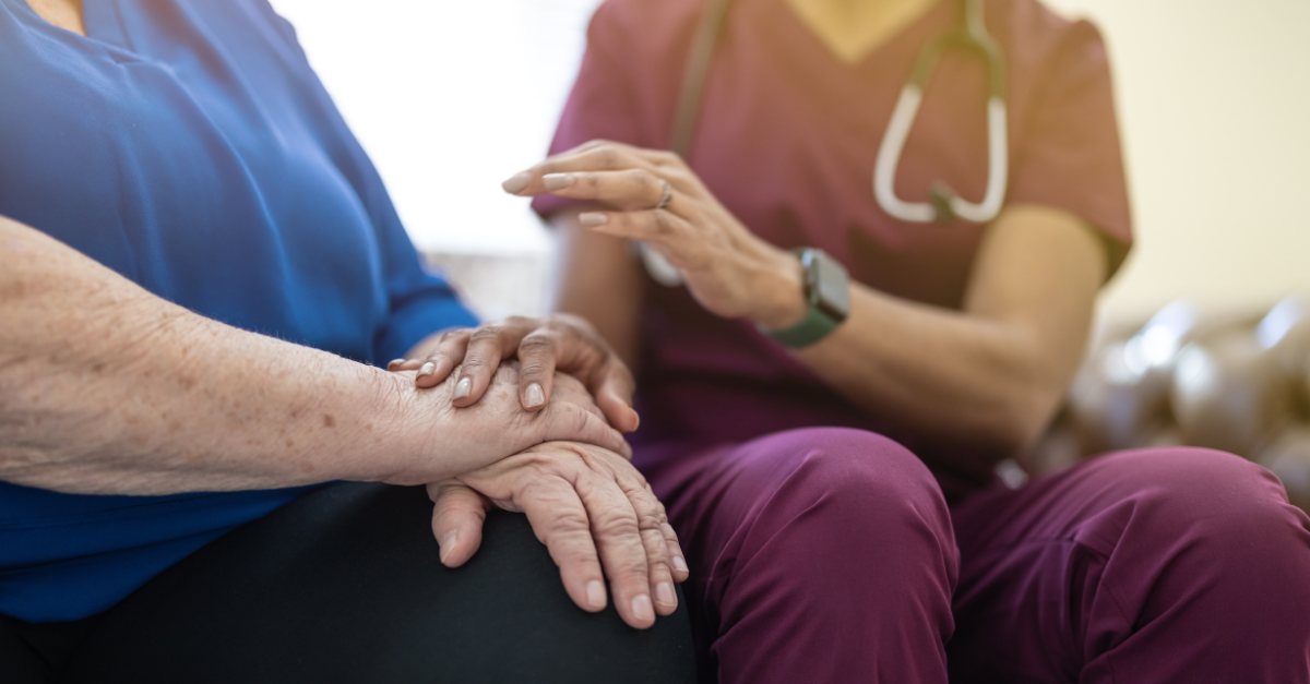 Eine Krankenschwester tröstet einen älteren Patienten und hält ihm die Hand.