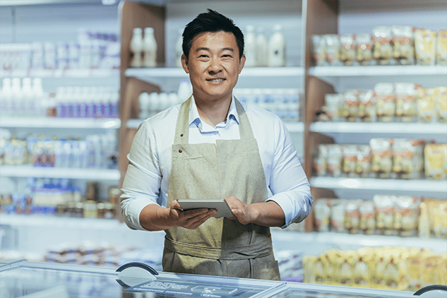 Asiatischer Mann, der lächelnd in die Kamera schaut und ein Tablet hält, während er in einem Schaufenster steht