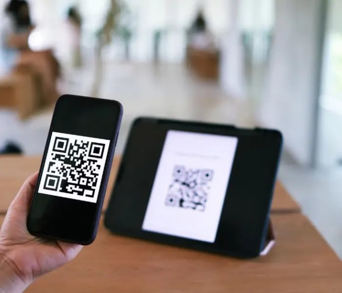 Person scannt QR-Code auf Tablet mit iPhone 