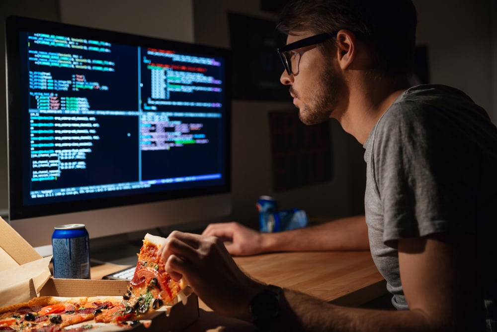 Profil eines konzentrierten jungen Softwareentwicklers, der Pizza isst und zu Hause programmiert