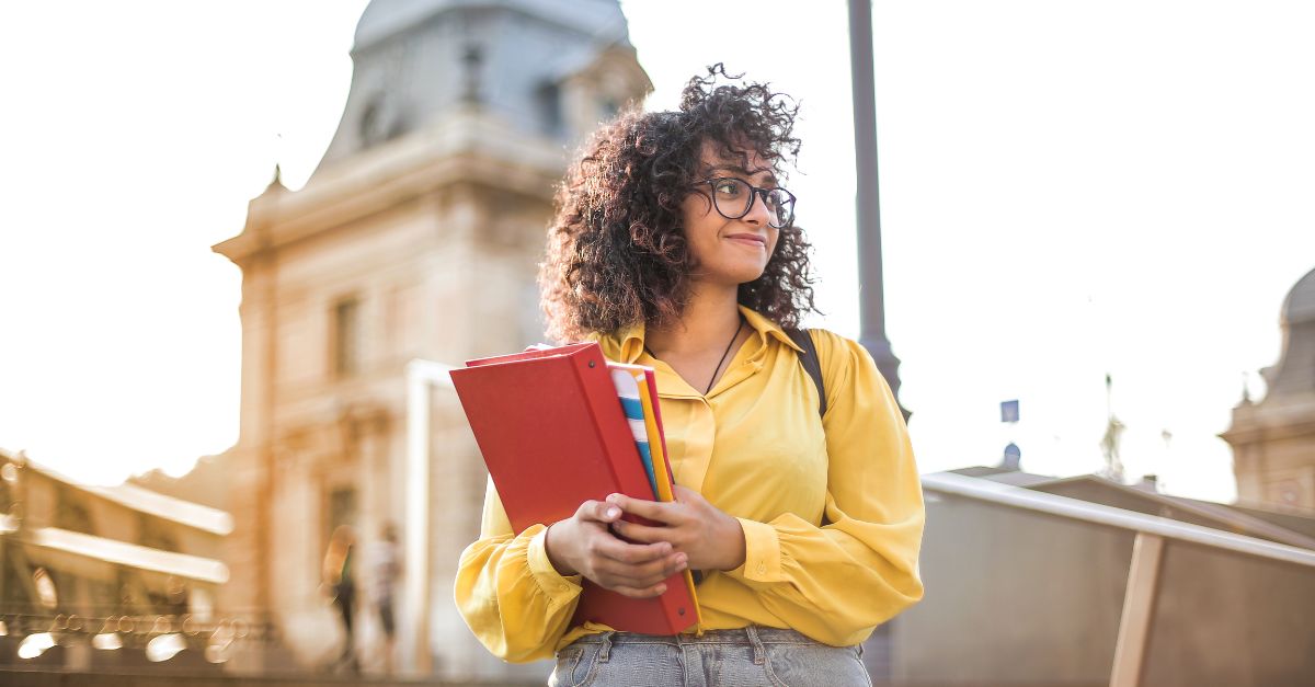 Studentin mit Büchern vor einem College-Gebäude 